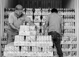 Workers organizing bottled drinks in shipping container.